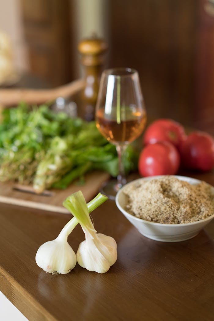 A culinary arrangement featuring fresh garlic, tomatoes, and herbs with a glass of wine.