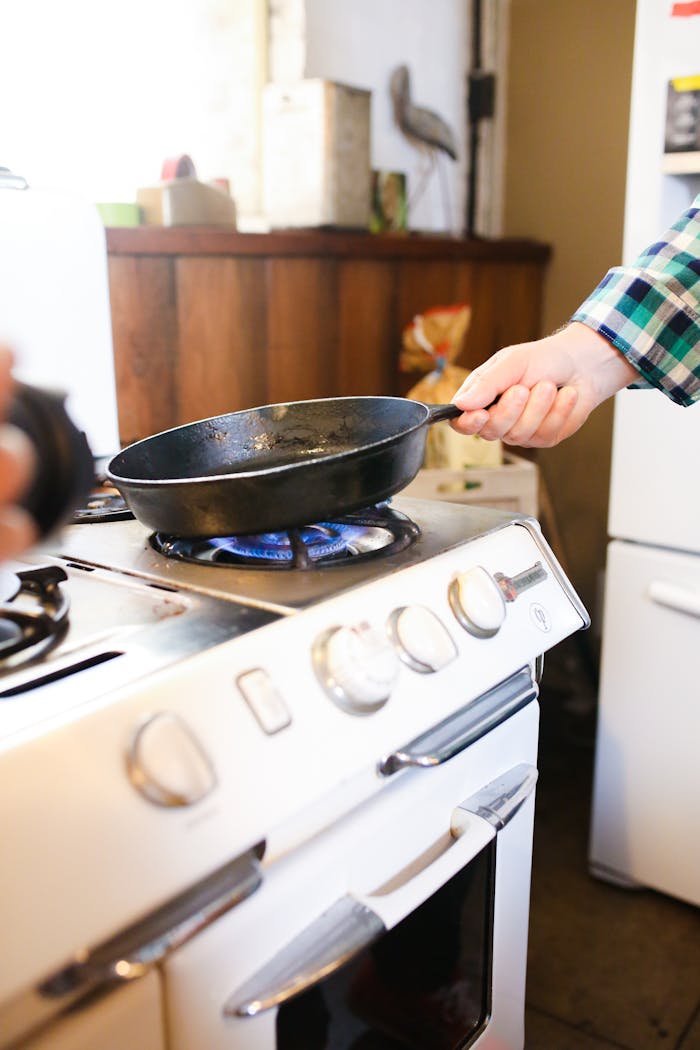services-04 Close-up of frying pan on stove with gas flame in cozy kitchen setting.