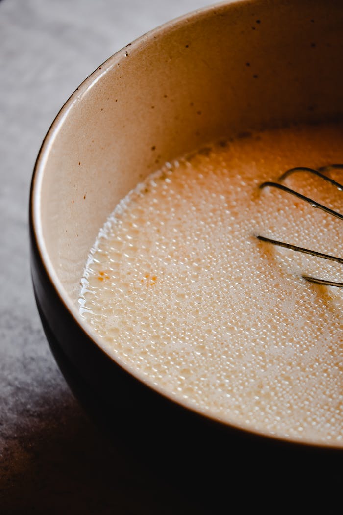 Close-up of bubbly pancake batter in a ceramic bowl with a whisk, perfect for cooking enthusiasts.